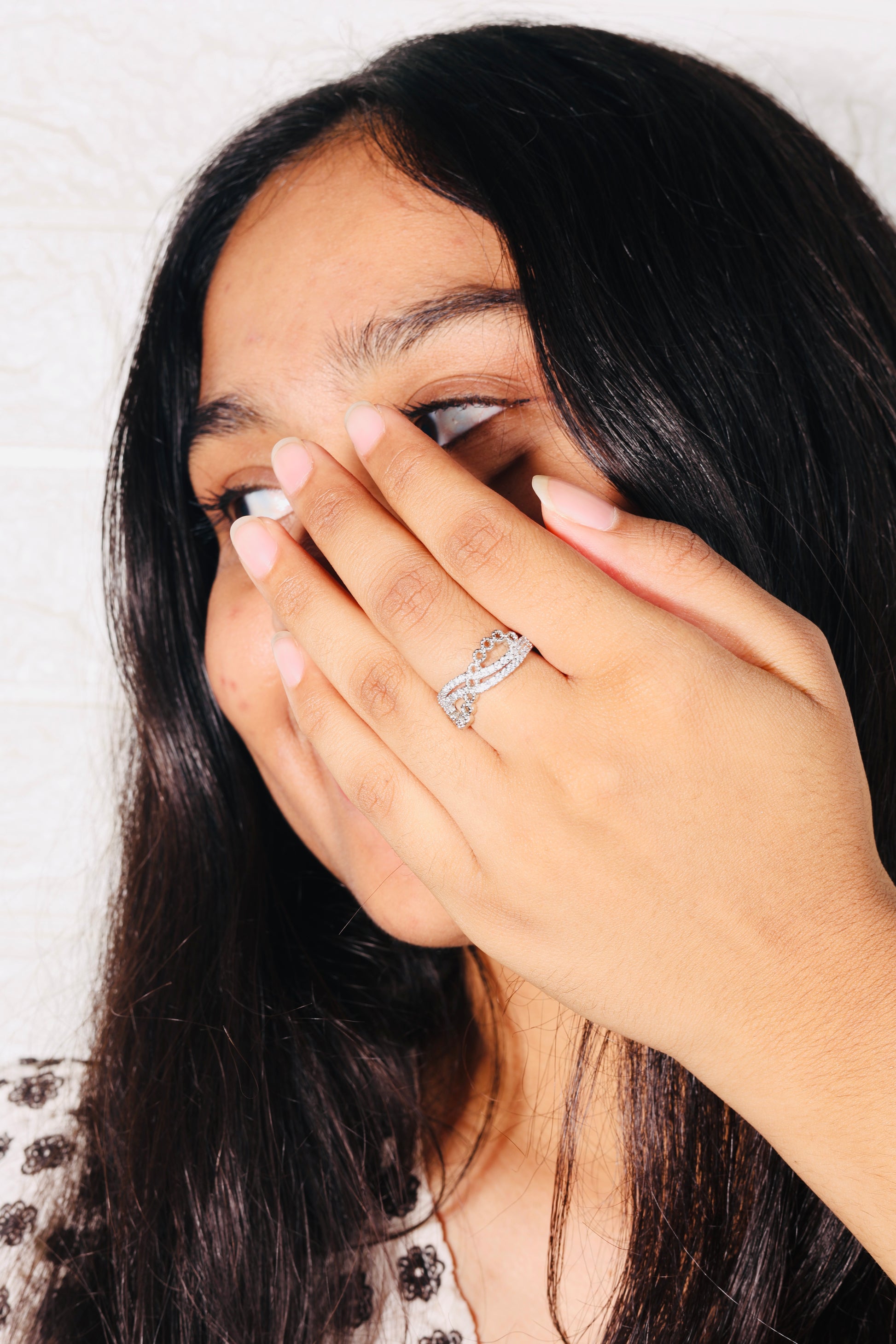 Person with long dark hair covering one eye, wearing a ring on their finger.